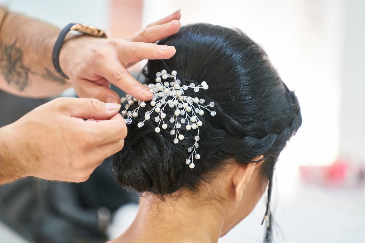 Photograph of a hairstylist arranging an elegant updo embellished with delicate decorative pins in a professional studio.