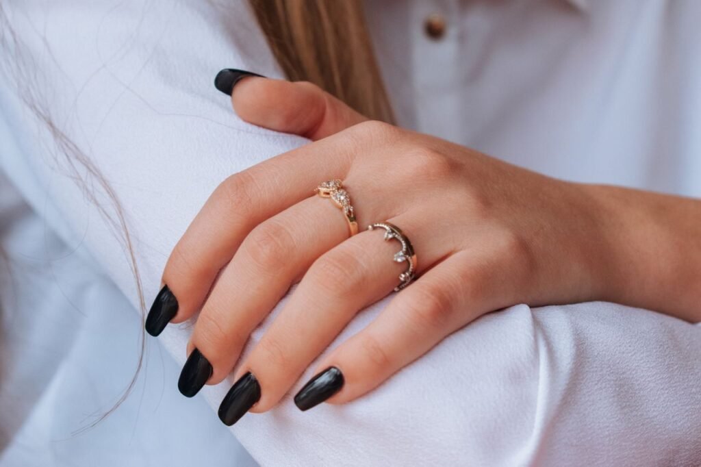 The Art of Drawing Readers In: Your attractive post title goes here Close-up of hands with black nail polish and elegant rings against a white shirt backdrop.