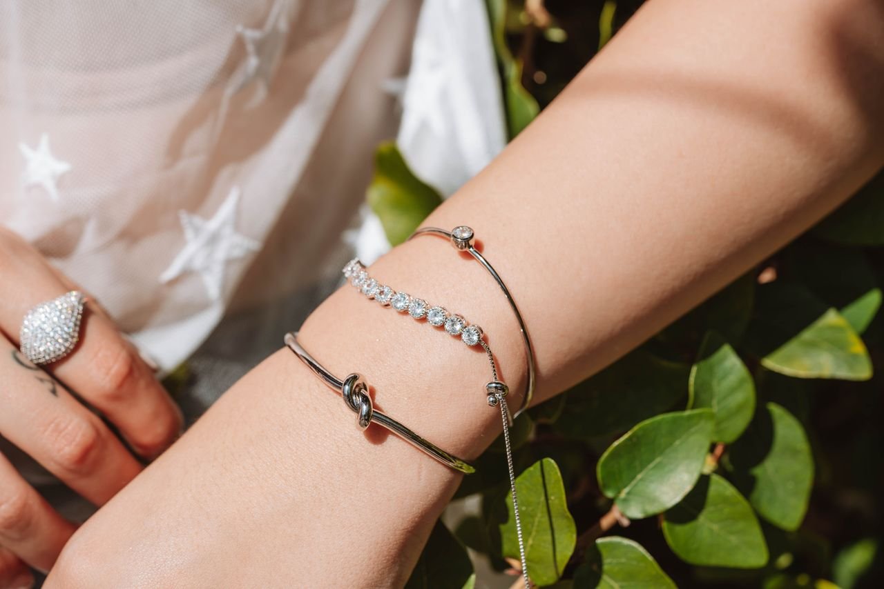 our-story-02 Close-up of elegant silver jewelry on wrist, featuring bracelets and a ring.